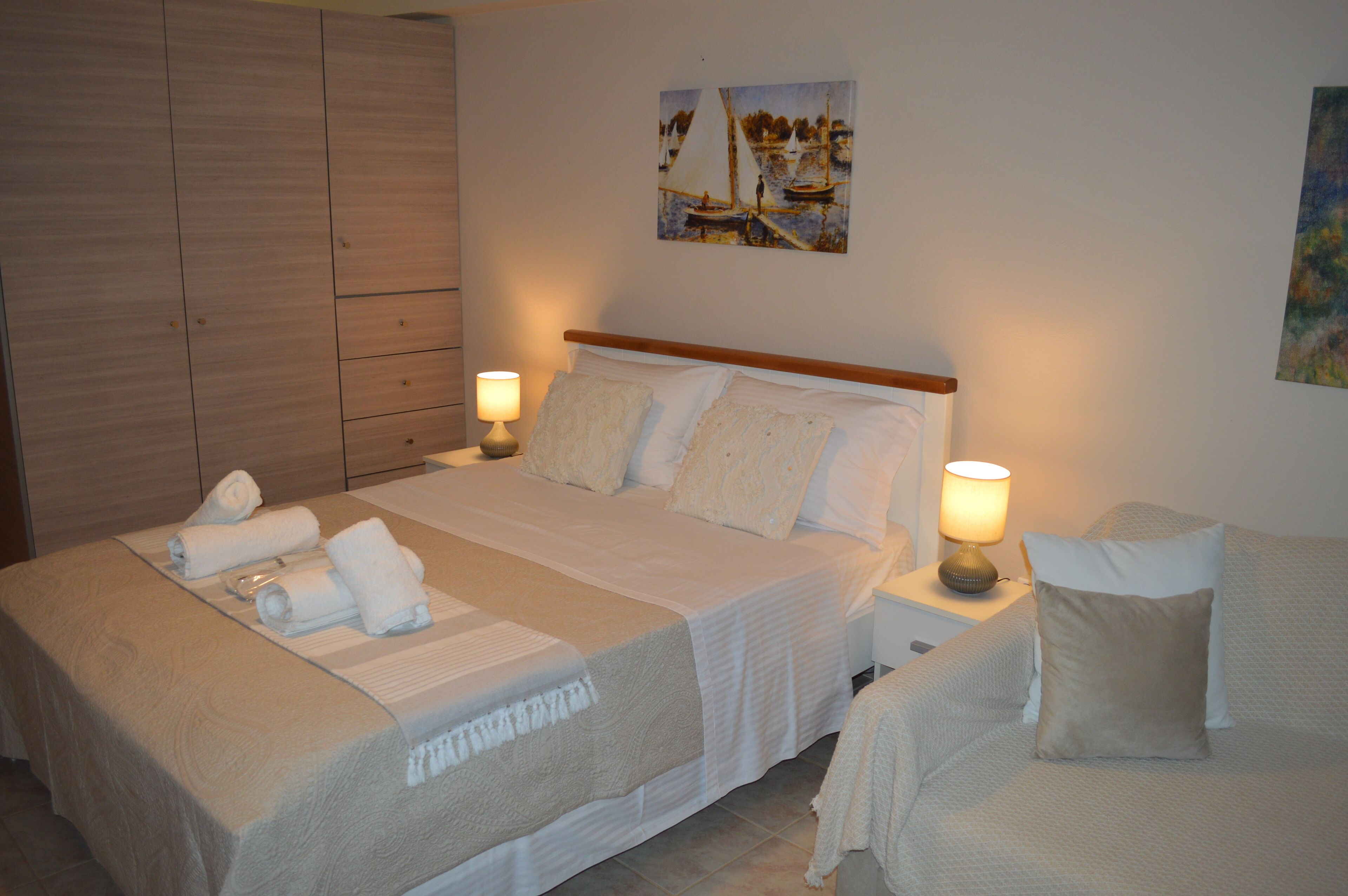 Un cuarto de hotel con una cama grande, dos mesitas de noche con lámparas, un armario de madera y un cuadro en la pared.