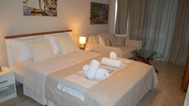 A hotel room with a large bed, two bedside tables, a chair, a glass table, and artwork on the walls. - Best House Petit Pylos Messinias (Pylos-Nestoras)