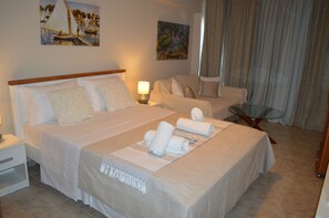 A hotel room with a large bed, two bedside tables, a chair, a glass table, and artwork on the walls. - Best House Petit Pylos Messinias (Pylos-Nestoras)