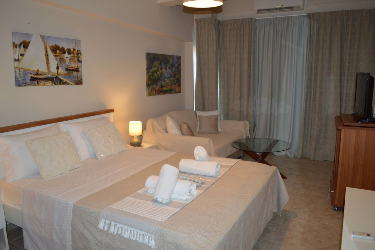 A hotel room with a large bed, a bedside table with a lamp, a chair, a TV, and a painting on the wall.