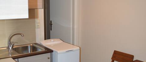 A compact kitchen with a sink, a small refrigerator, and a dining area with wooden chairs.
