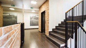 A modern interior with a brick wall, a staircase with black railings, and directional signs on the ceiling. - Stylish Apartment near the Station | Parking | Balcony (Kraków)