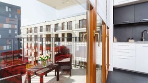 A modern apartment with a balcony, a dining area with red furniture, and a kitchen with white cabinets. - Stylish Apartment near the Station | Parking | Balcony (Kraków)