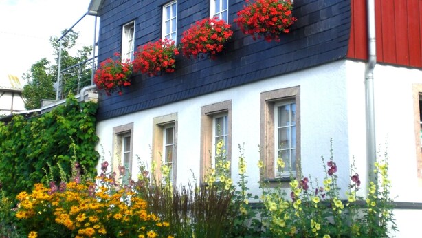 Un bâtiment à deux étages, à la façade bleu foncé rehaussée d’éléments rouges, et doté de nombreuses fenêtres ornées de jardinières.