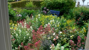 Un jardin agrémenté de diverses fleurs et muni d’un banc.