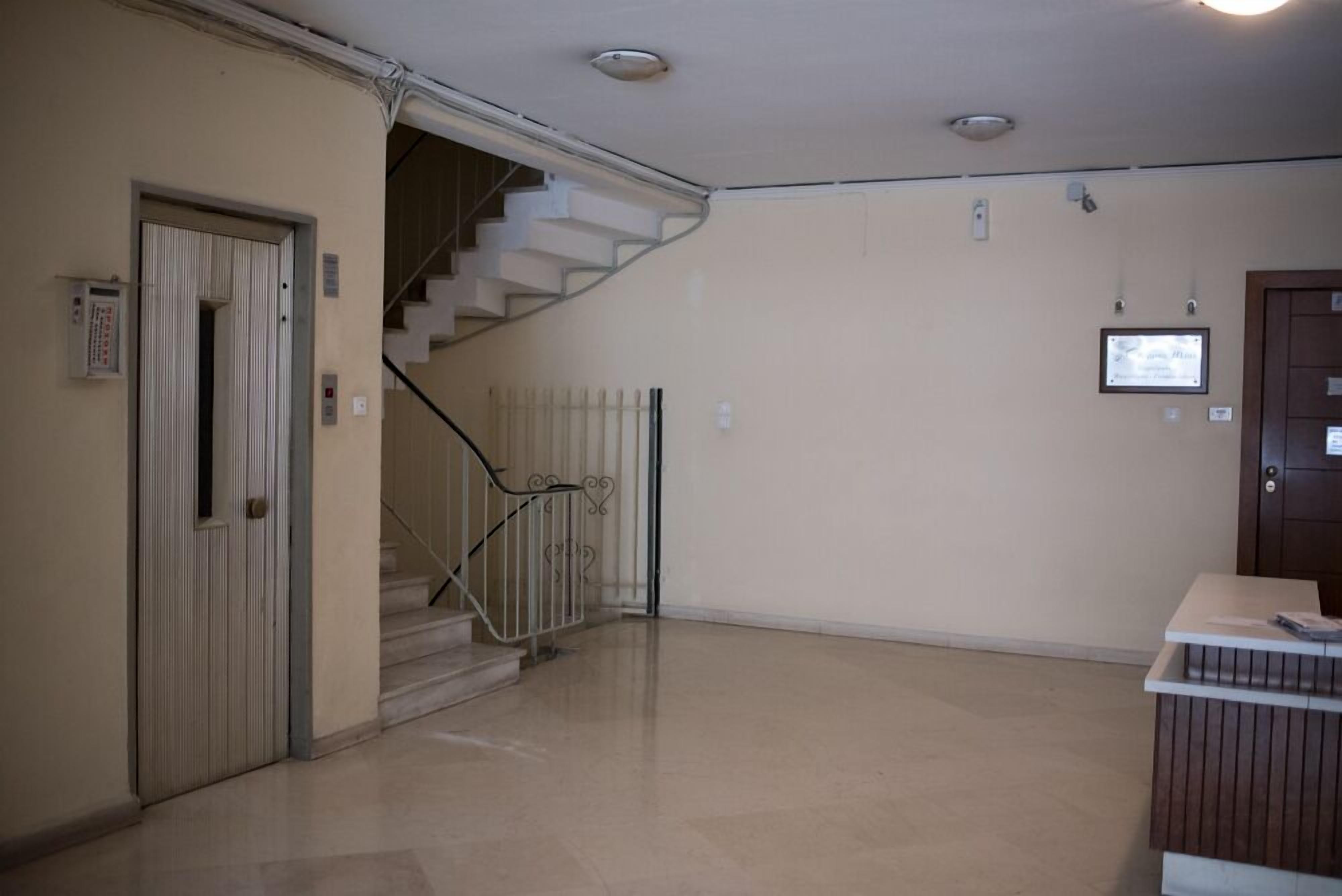 A spacious room with a staircase, a reception desk, and a door with a security panel.