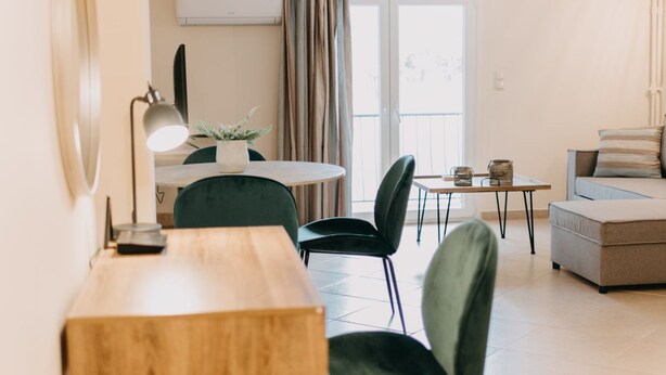 A modern living room with a dining area, featuring a wooden table, green chairs, a sofa, and a small side table. - Best House Central Luxury Apartment (Patras)