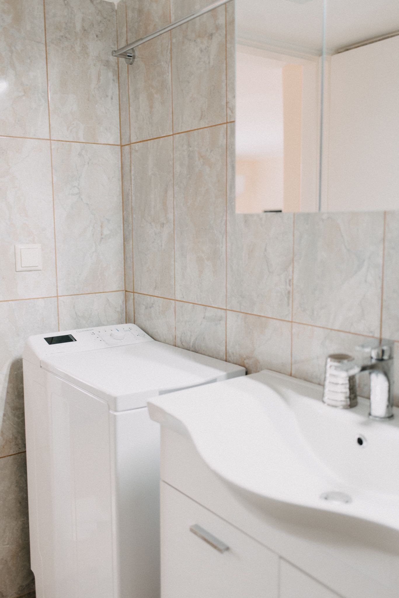Un baño con lavadora blanca, un lavabo y un espejo.