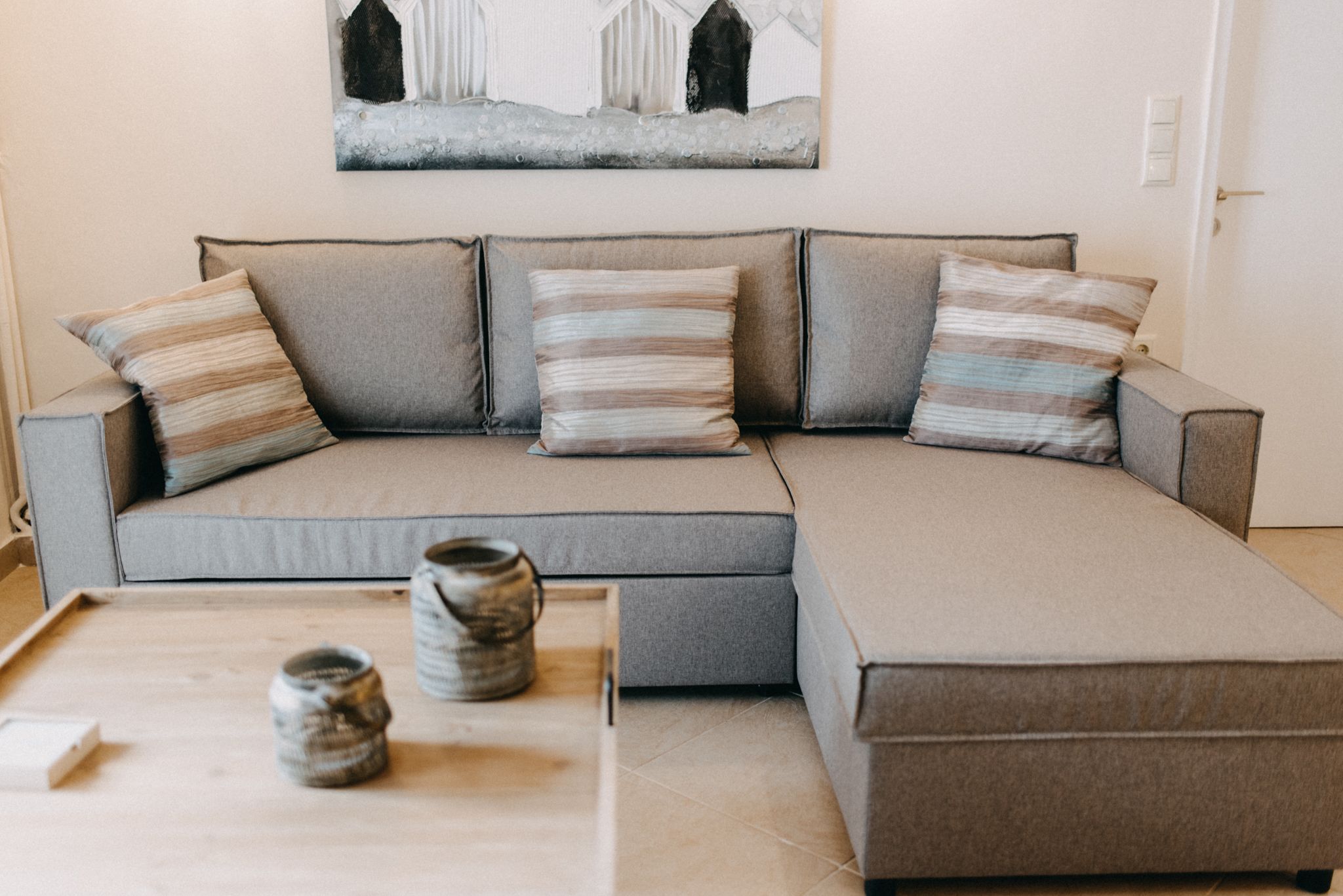 A modern living room with a grey sectional sofa, three striped pillows, and a small wooden table with two ceramic jars.