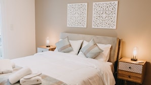 A neatly made bed with white linens and striped pillows, two bedside tables with lamps, and decorative wall art. - Best House Central Luxury Apartment (Patras)