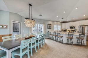 A modern kitchen with a dining area, featuring a central island, bar stools, and a chandelier. - The Tappan at Ships Watch in Duck (Duck)