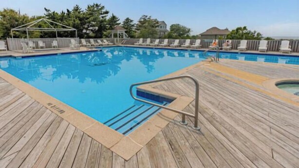 En træterrasse med swimmingpool, liggestole og et overdækket område.