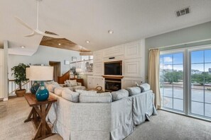 A spacious living room with a sectional sofa, a television, and a large window offering a view of the outdoors. - The Tappan at Ships Watch in Duck (Duck)