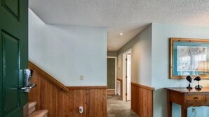 A hallway with wooden paneling, a staircase, a desk with a lamp, and a framed picture on the wall.