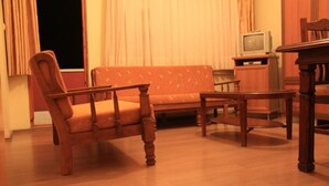 Una habitación con una silla de madera, una mesita pequeña, un sofá y un televisor sobre un mueble.