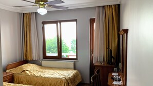 Habitación de hotel con dos camas, un escritorio, una silla, un ventilador de techo y una ventana con cortinas.