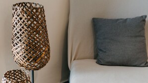 Una sala moderna con un sofá gris, una almohada gris y dos lámparas de pie tejidas sobre soportes de metal.