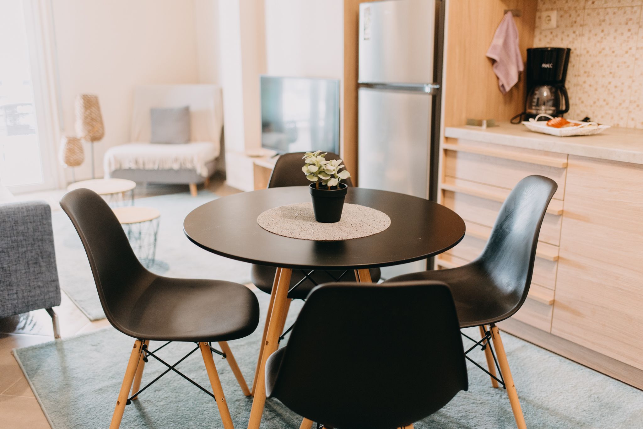 A modern kitchen with a round table, black chairs, and a potted plant.