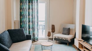 Una sala de estar moderna con un sofá, una silla, una mesita redonda y un televisor sobre un mueble de madera.