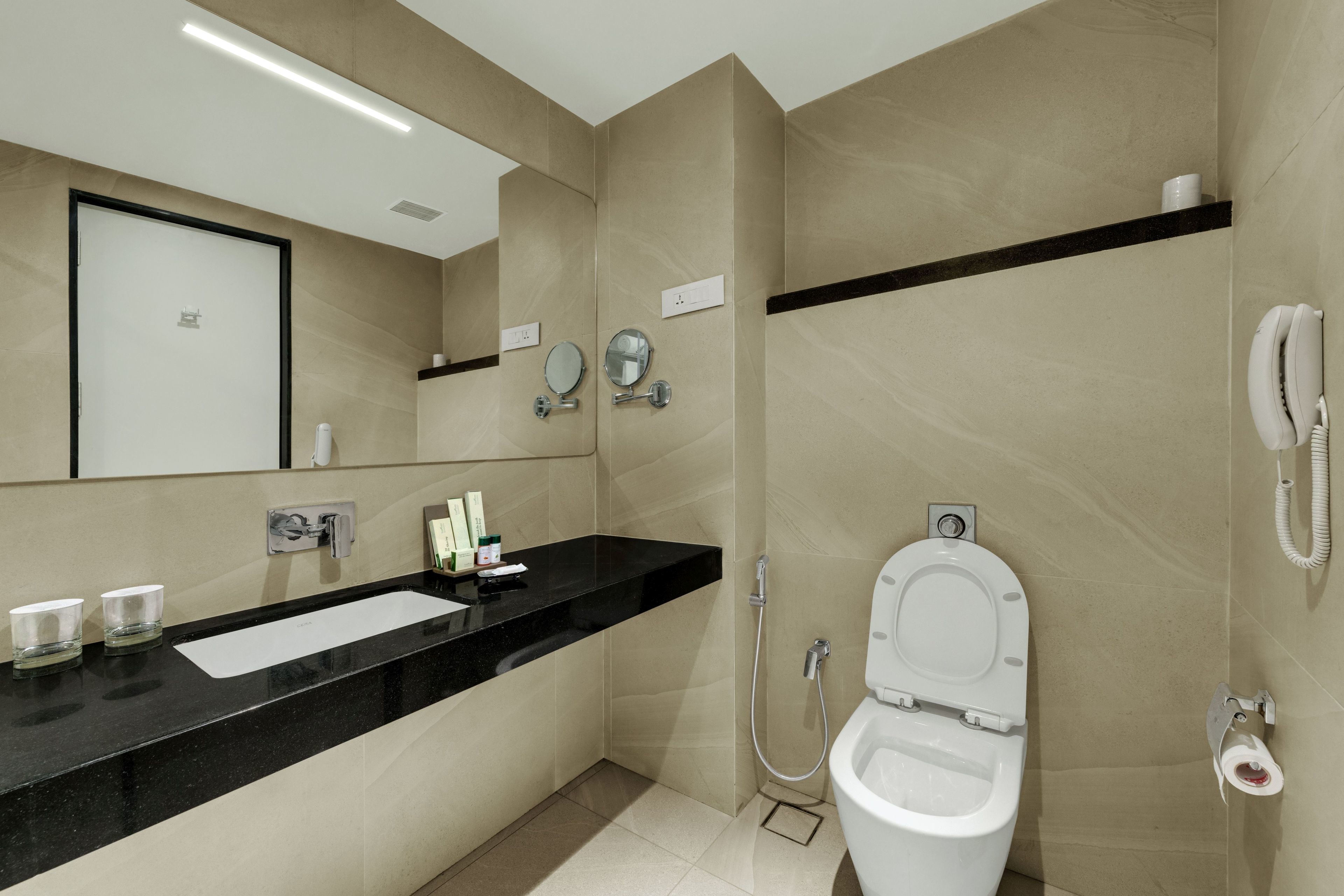 A modern bathroom with a black countertop, a white toilet, a sink, a mirror, and a telephone.