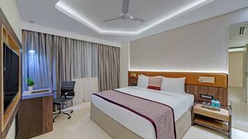 Camera d'albergo con un letto, una scrivania, una sedia, una televisione e un comodino con bottiglie.