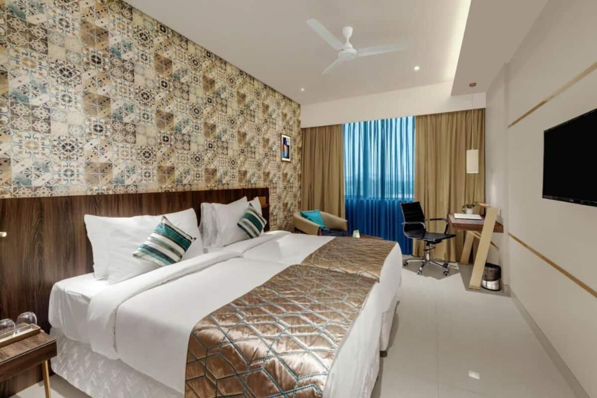A hotel room with a large bed, a desk with a chair, a television, and a ceiling fan.