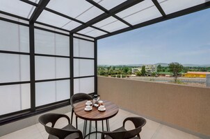 Un balcón con una mesa dispuesta para dos, vista a un paisaje urbano y cielo despejado.
