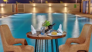 Mesa junto a la piscina con una botella, vasos y una porción de pastel, rodeada por dos sillas.