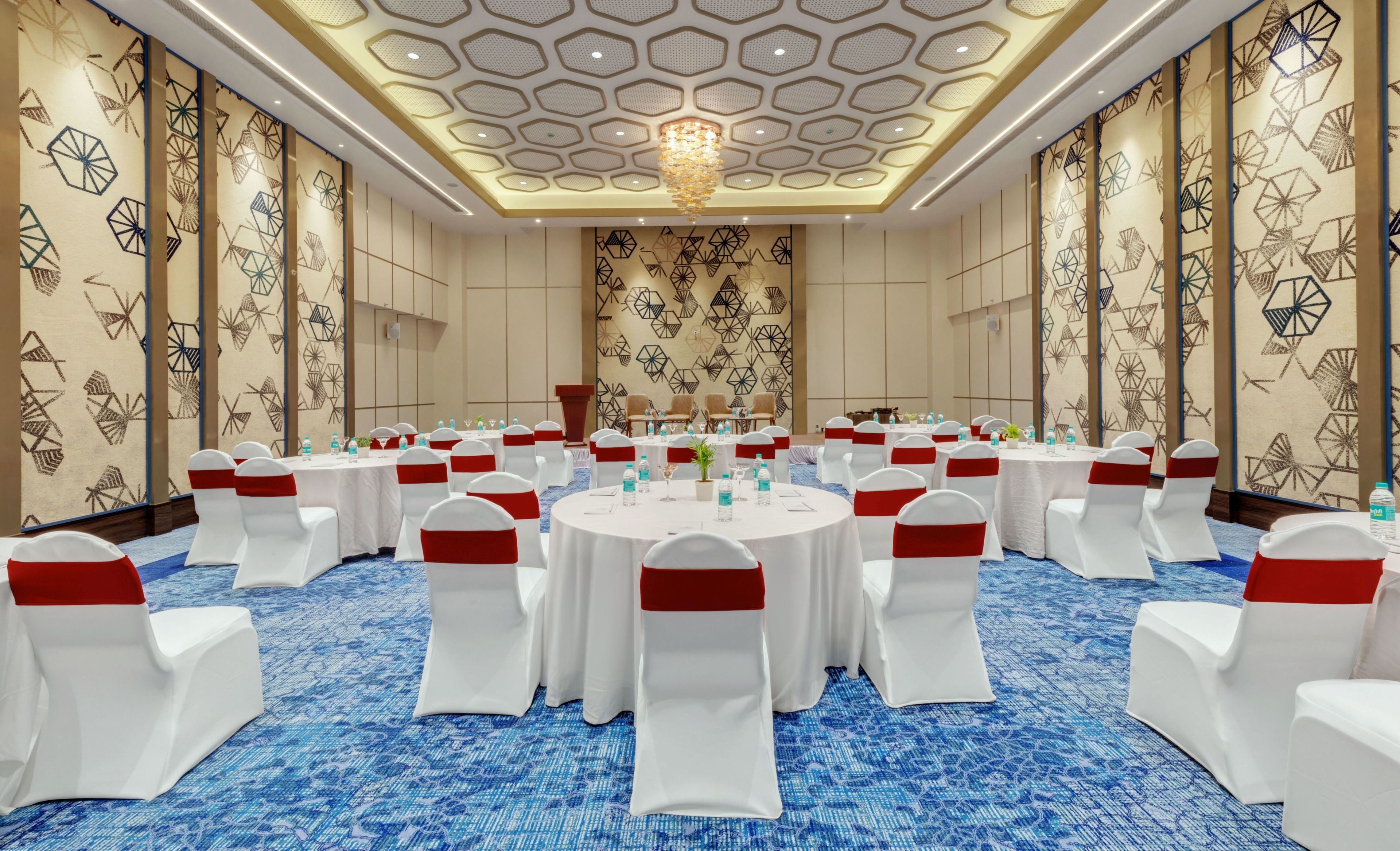 A conference room with round tables, white chairs with red sashes, and a blue carpet.