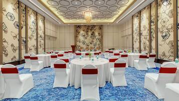 A conference room with round tables, white chairs with red sashes, and a blue carpet.