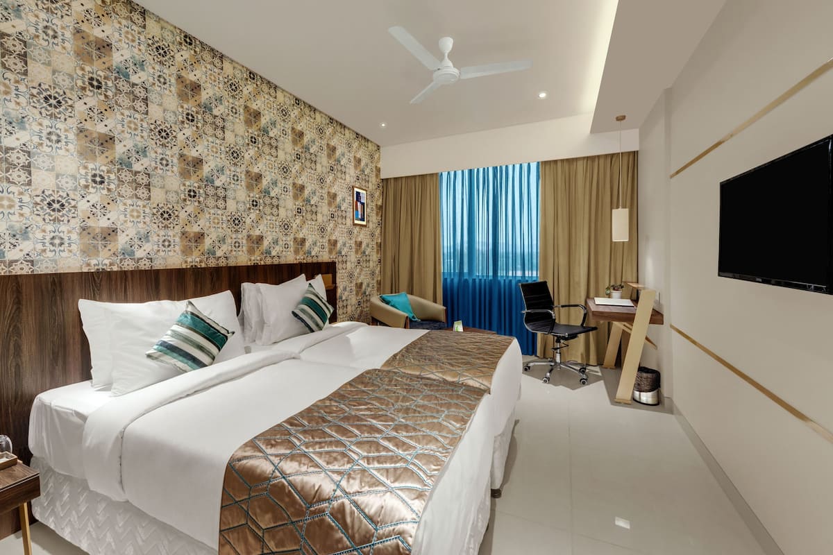 A hotel room with a bed, a desk, a chair, a television, and a window with curtains.