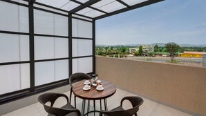 Un balcón con una mesa dispuesta para dos, vista a un paisaje urbano y cielo despejado.
