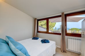 A bedroom with a bed, two pillows, a window with curtains, and a view of the sea. - Cupido (Gardone Riviera)