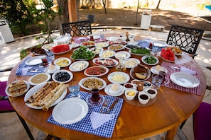 Una mesa de madera redonda dispuesta para una comida, con diversos platos y bebidas.