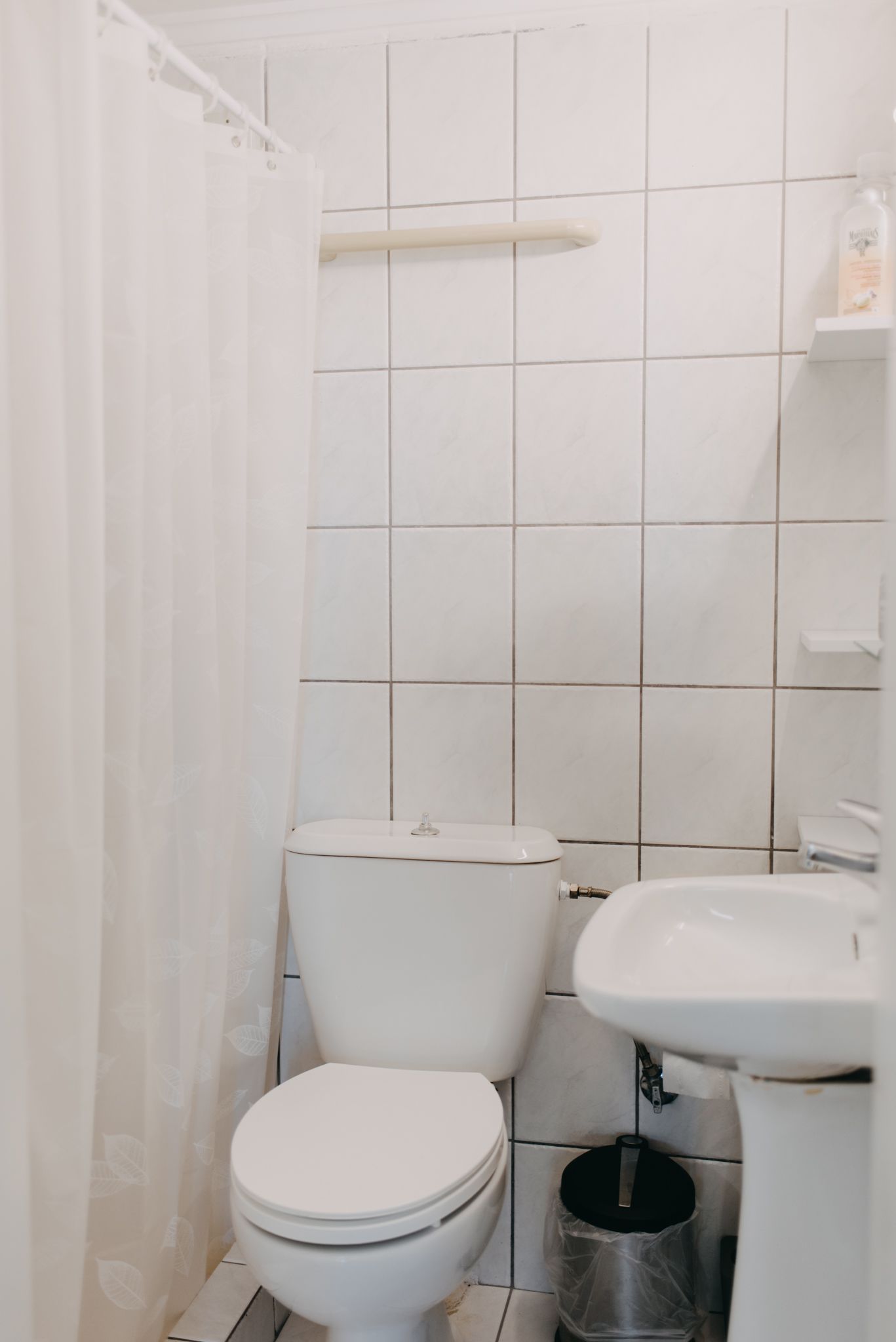 Une petite salle de bain propre, équipée de toilettes, d’un lavabo et d’un rideau de douche.