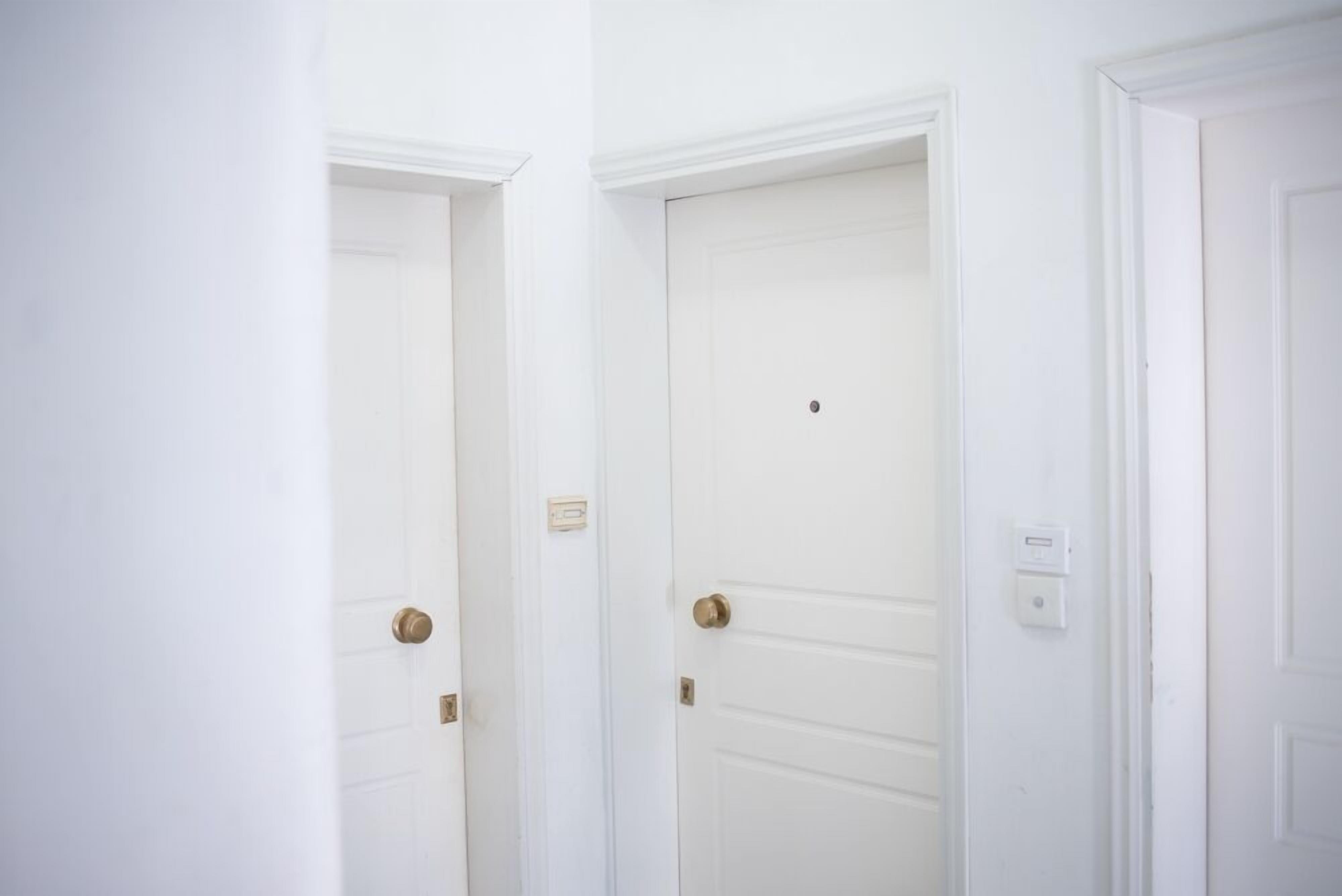 Un pasillo con puertas blancas, cada una con un picaporte de latón y un interruptor de luz pequeño encima de la puerta.