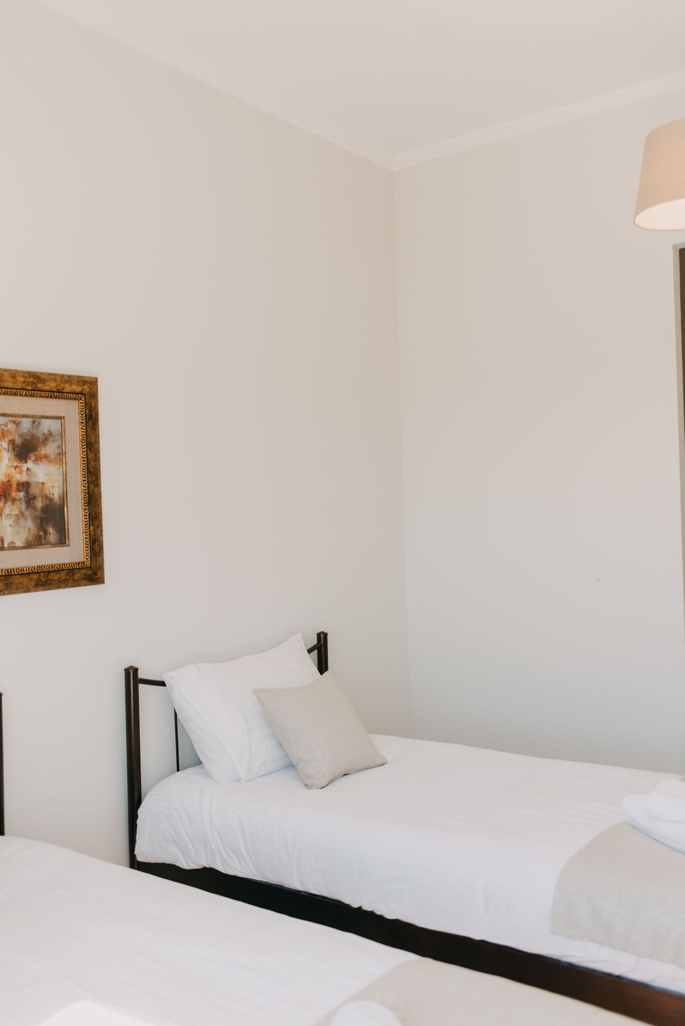 A single bed with white bedding in a room with white walls and a framed picture on the wall.