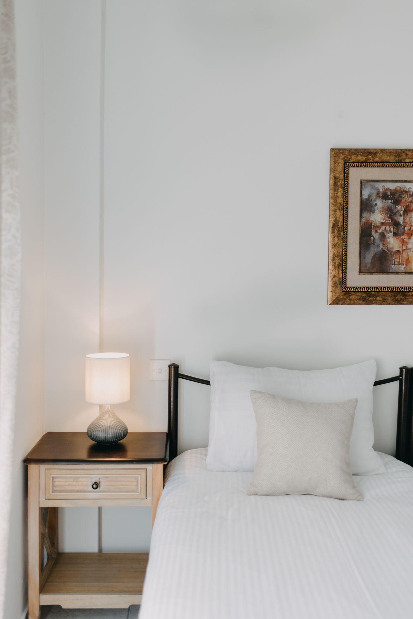 Un letto rifatto con lenzuola bianche, una lampada da comodino e un quadro appeso al muro.