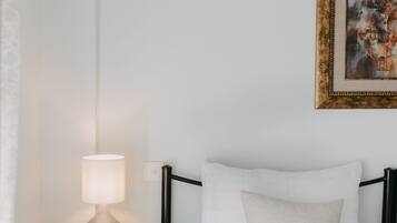 Un letto rifatto con lenzuola bianche, una lampada da comodino e un quadro appeso al muro.