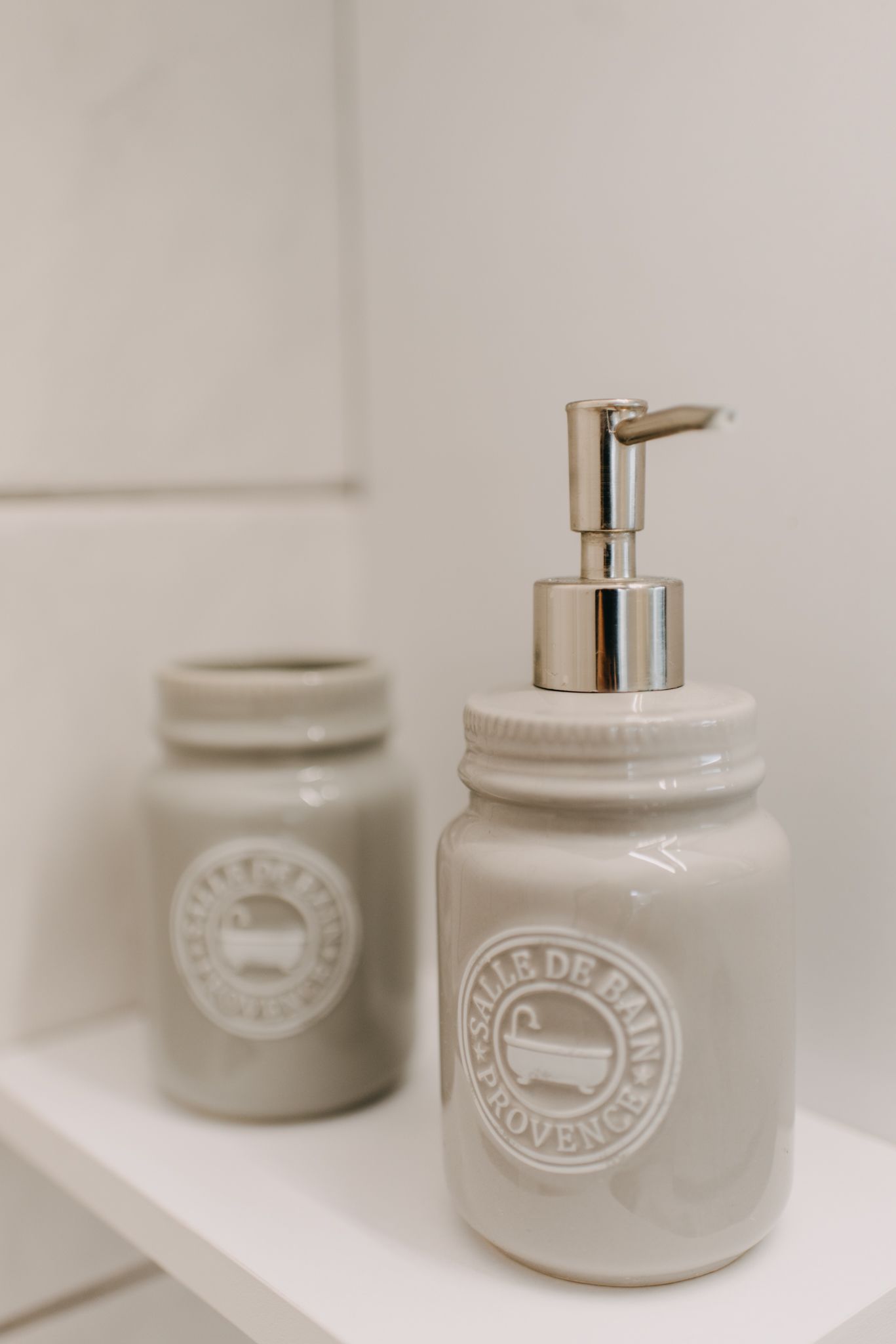 Two white ceramic jars with pump dispensers on a white shelf.