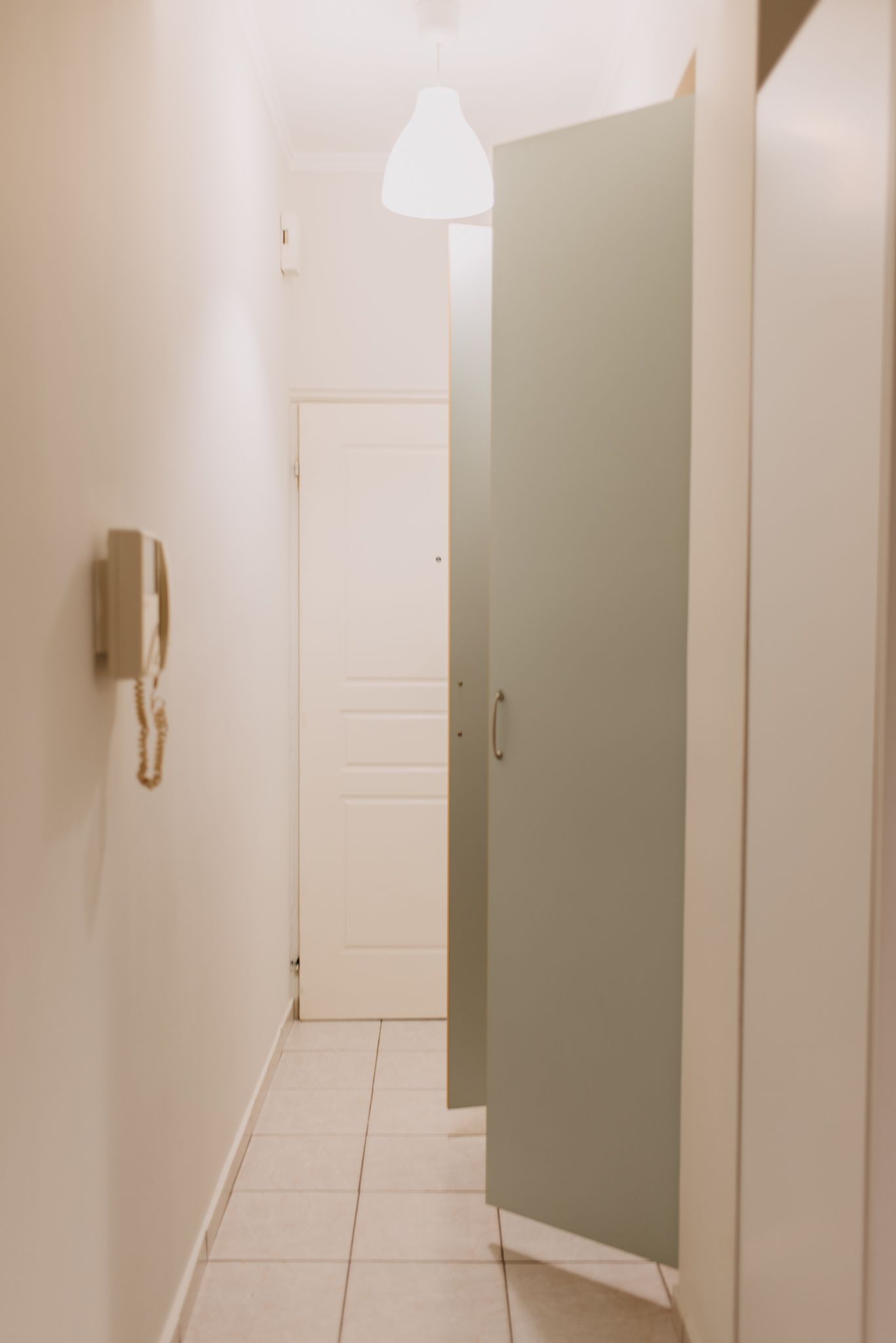 Un pasillo con una puerta blanca, un teléfono de pared y una lámpara en el techo.