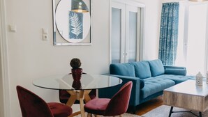 A modern living room with a blue sofa, a glass dining table with two red chairs, and a white coffee table.