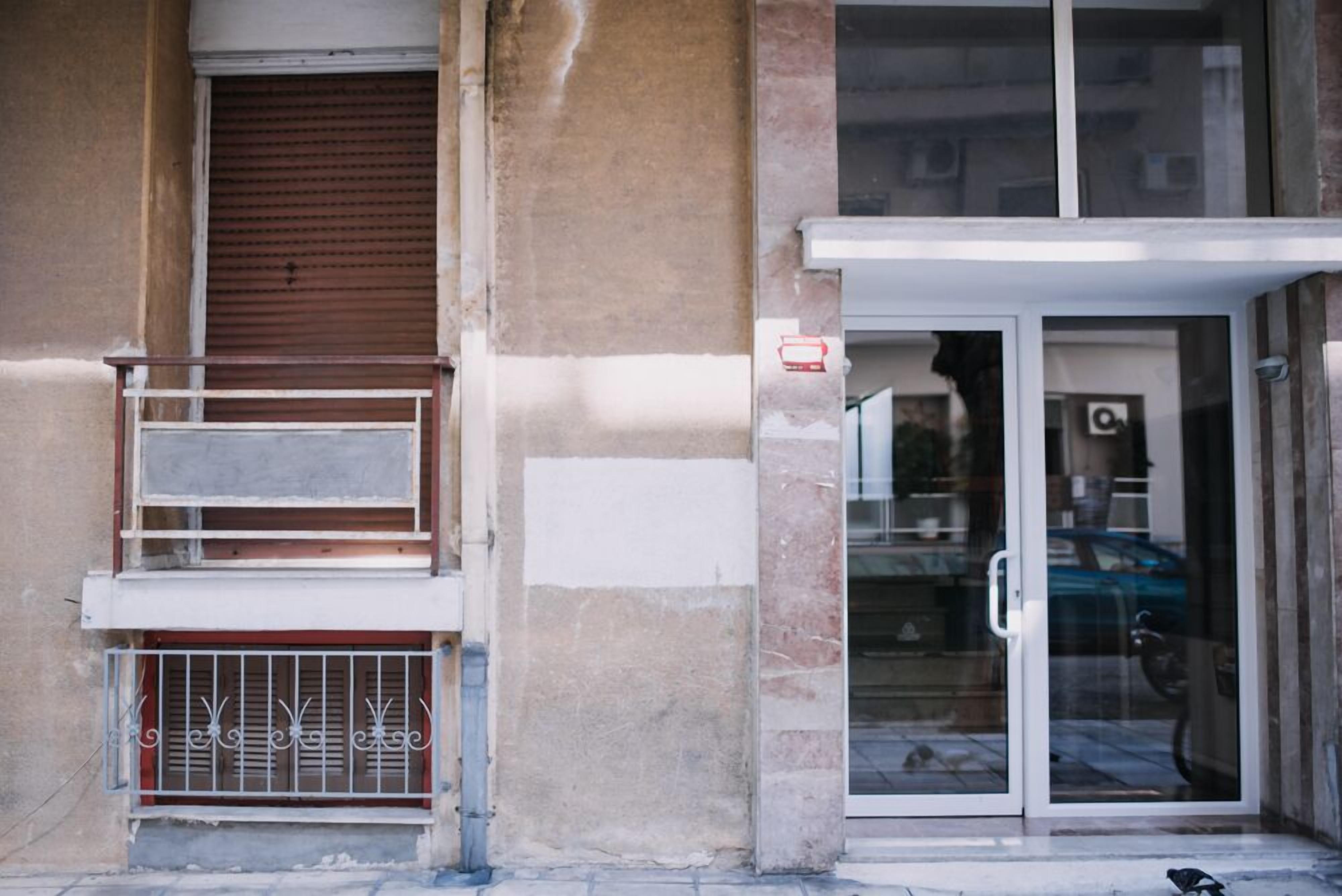 A building facade with a closed shutter, a metal balcony, and a glass door entrance.