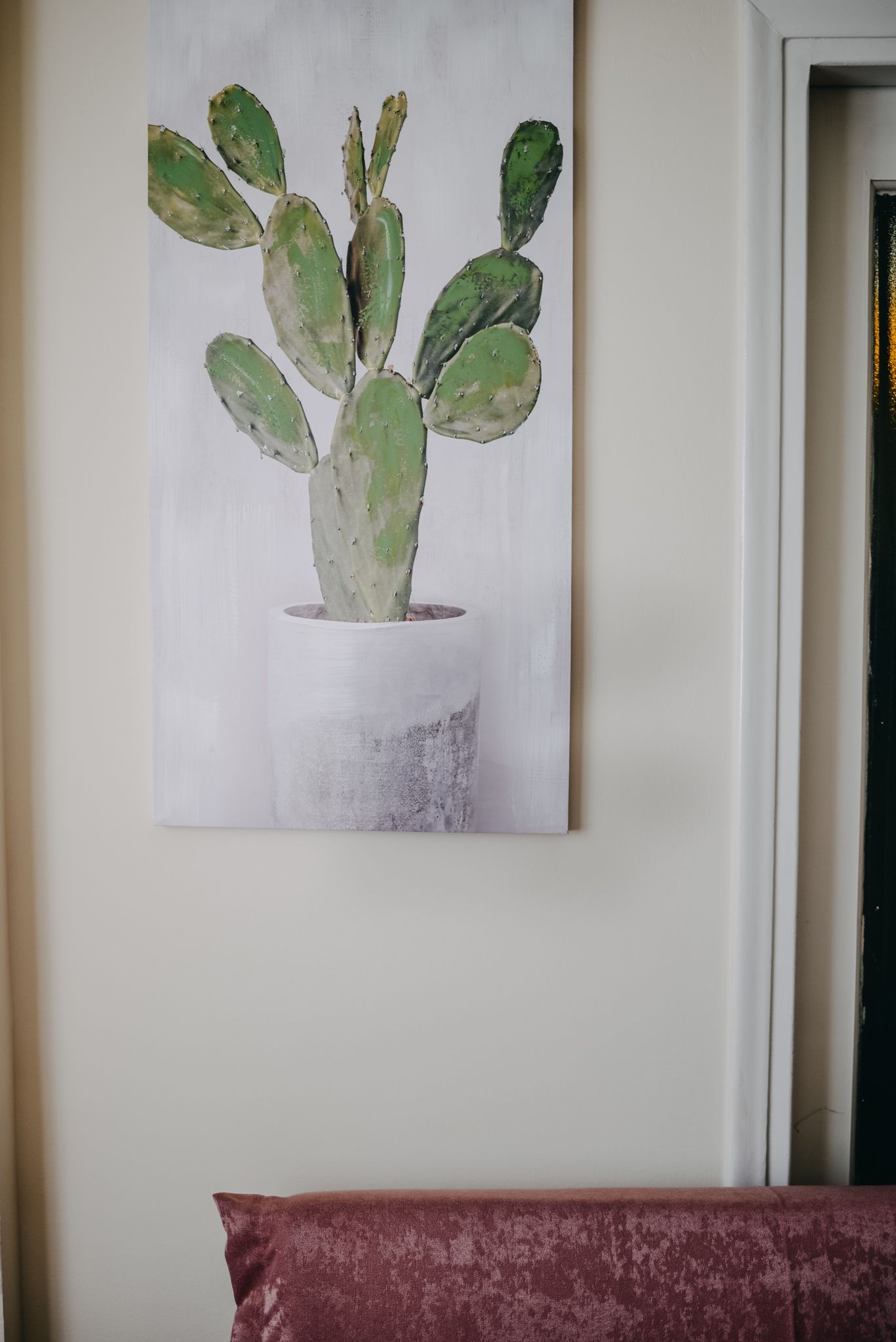 Una pintura d'un cactus en una testra blanca penjada a la paret.