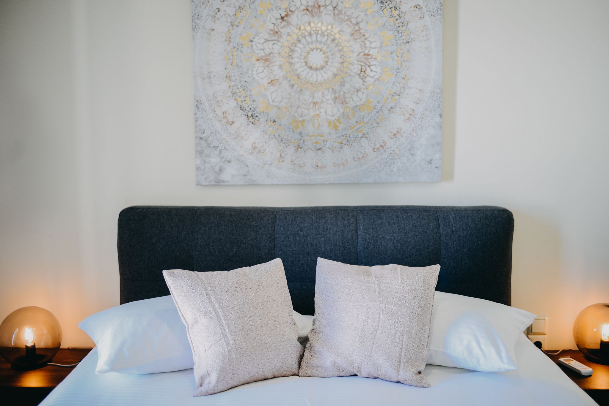 Un letto rifatto con due cuscini, una testata scura e un quadro astratto appeso alla parete.