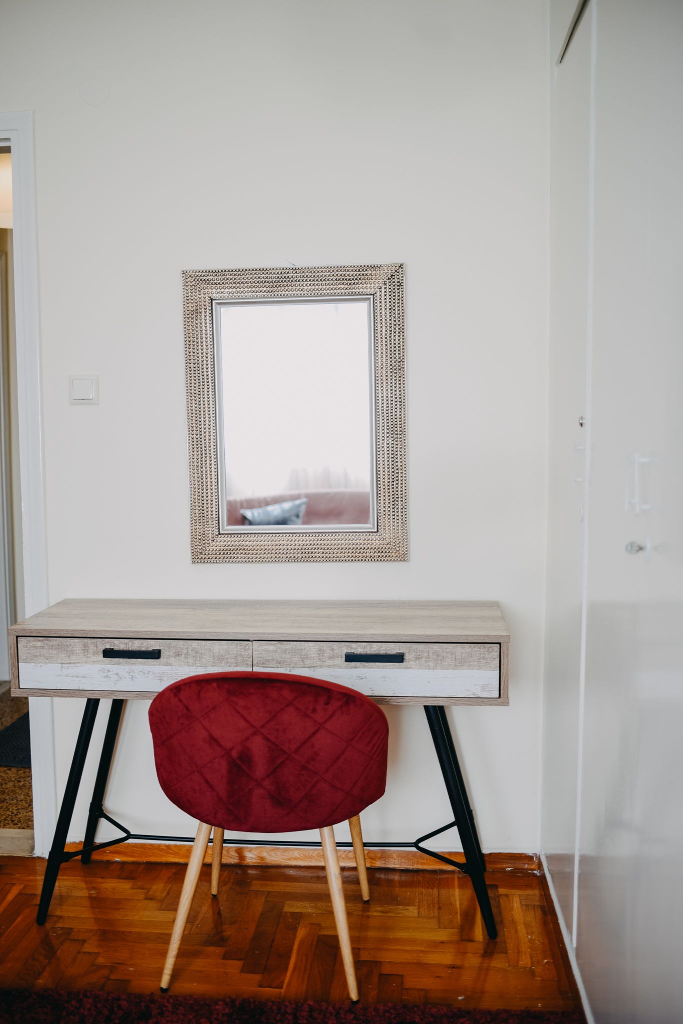 Um quarto com uma escrivaninha de madeira, uma cadeira vermelha e um espelho emoldurado na parede.
