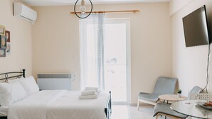 Habitación de hotel con cama, una silla, una mesa, televisor y vistas al balcón.
