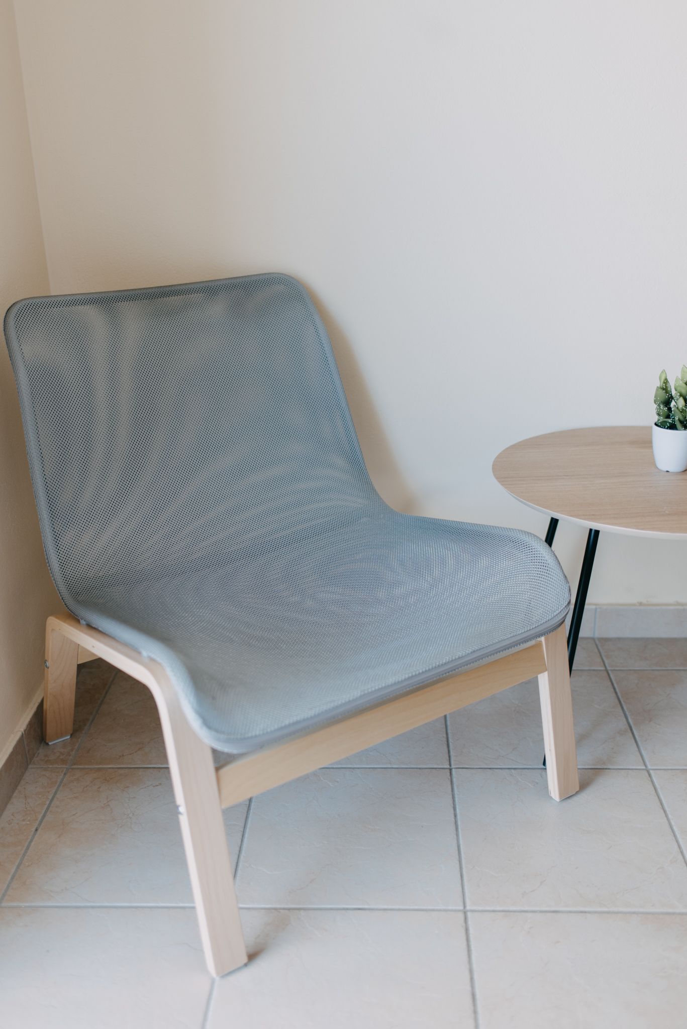 A modern chair with a light blue mesh backrest and seat, paired with a round wooden table beside it.