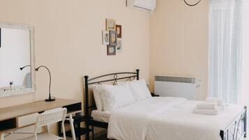 A bedroom with a bed, a desk, a chair, a mirror, and a wall-mounted air conditioner.
