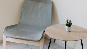 Una habitación moderna con un sillón tapizado gris, una mesita redonda con una planta en maceta y un banco acolchado gris.